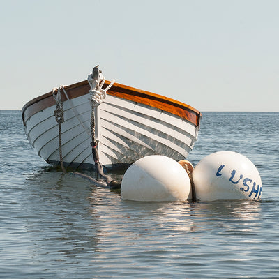 classic white wooden dinghy on a mooring ball.Tones of grays and blue calm seas with light gray sky