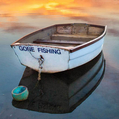 Stern view of the  Gone fishing rowboat at anchor with orange sunset sky reflected in the water